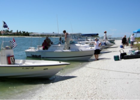 Photo, men and women in and around four boats pulled up to a Florida beach. Some are unloading things from the boats