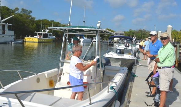 Photo, several boats tied to a dock and several adults standing on the dock and in one of the boats.