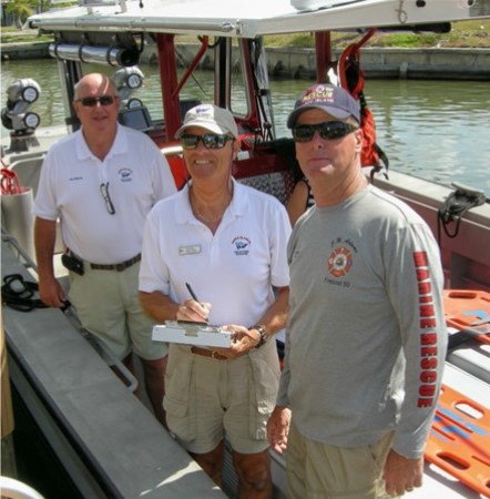 Three men standing in boat, one with clipboad and pen